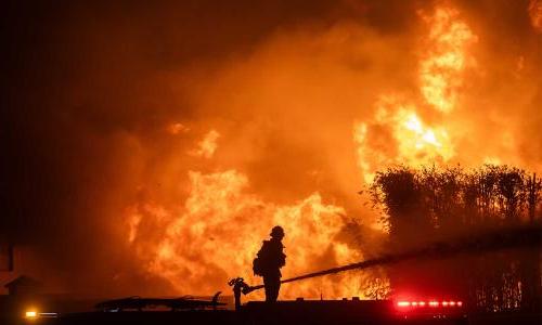 Firefighter standing on fire truck hosing down huge fire